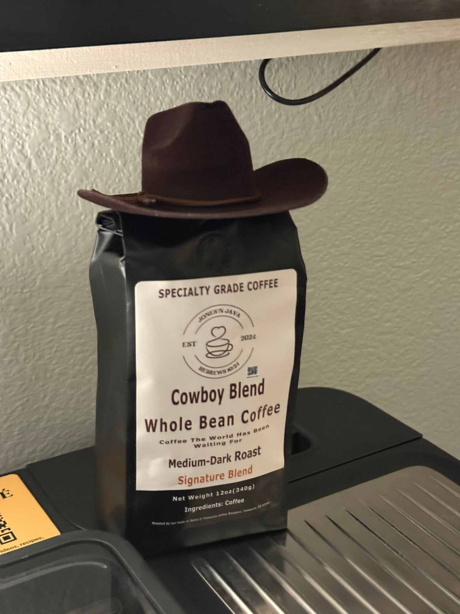 Coffee bag labeled “Cowboy Blend” with a cowboy hat resting on top, placed on a metal surface
