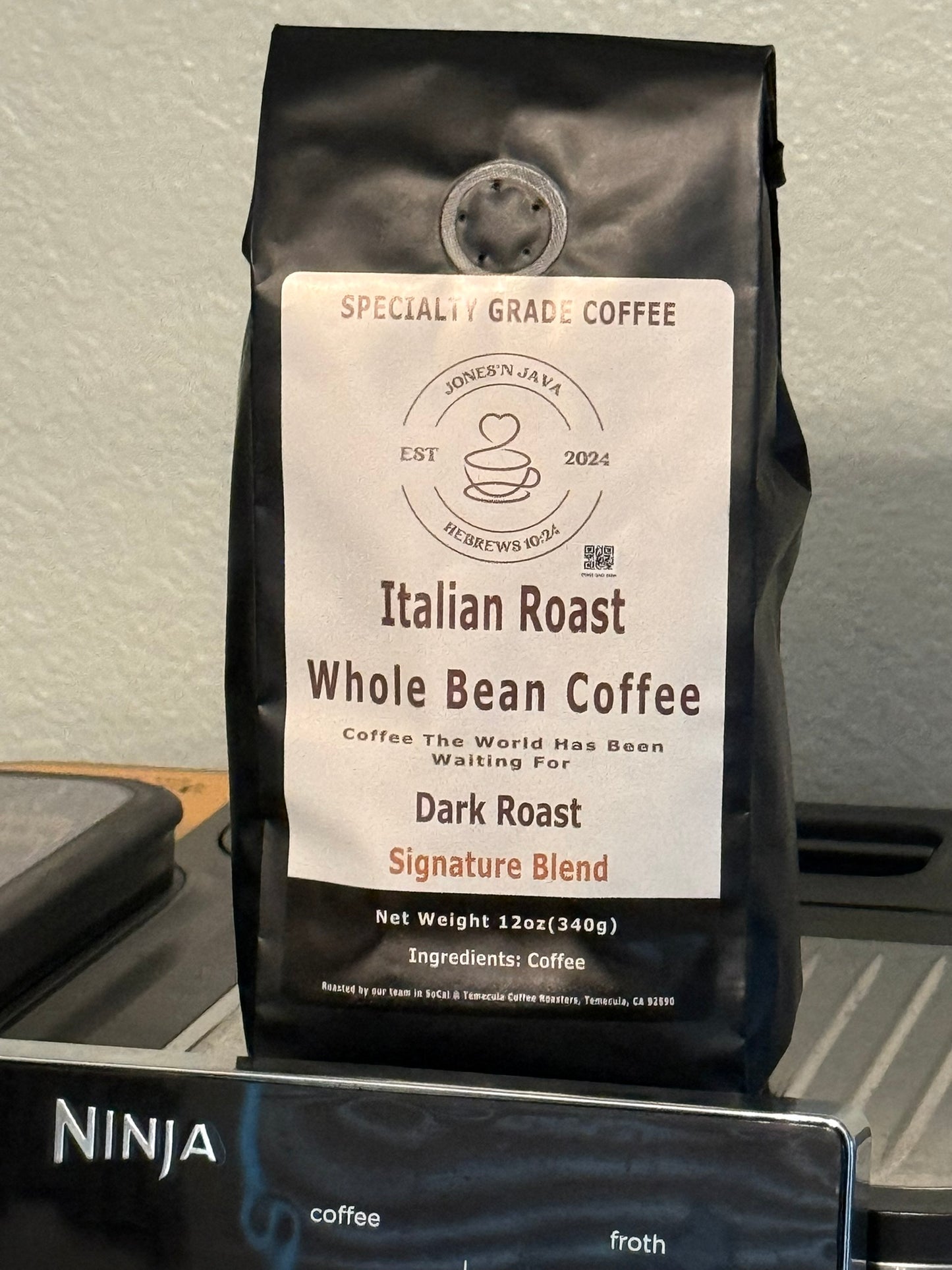 Italian Roast whole bean coffee by Jones’N Java on a kitchen counter with a coffee machine in the background.